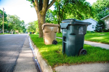 Tan garbage bin and green recycling bin on the curb.